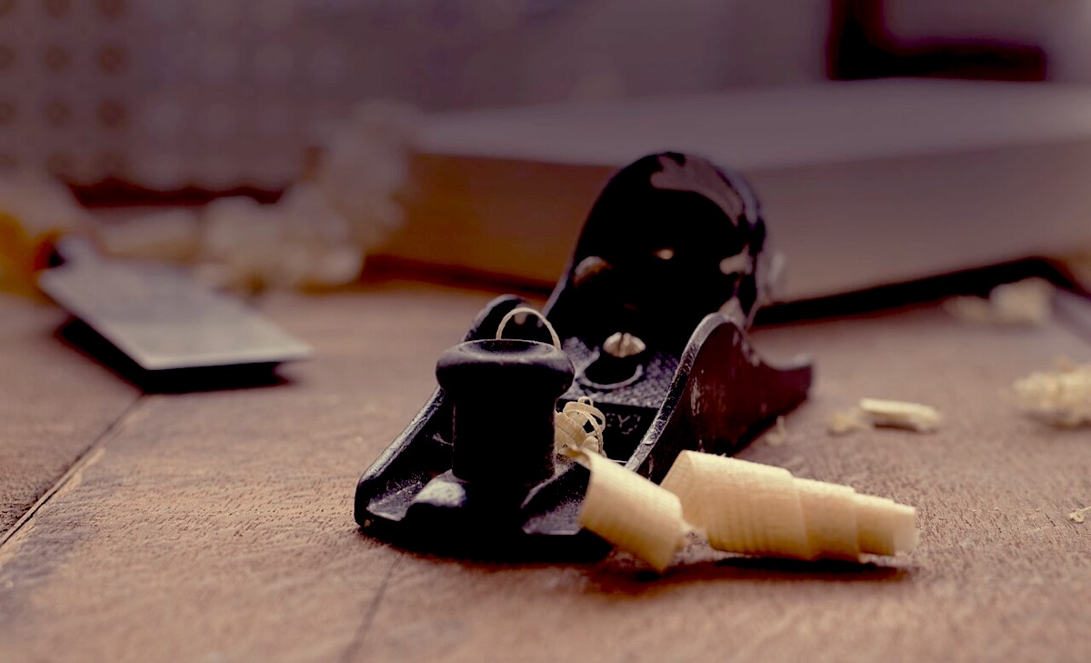 A hand plane and fresh wood shavings on a workbench