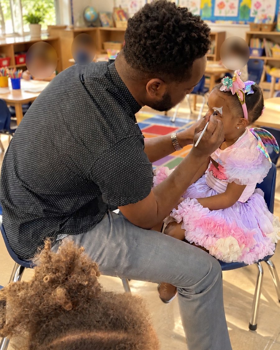 Michael Olaiya face-painting a young girl in a unicorn headband at a classroom celebration