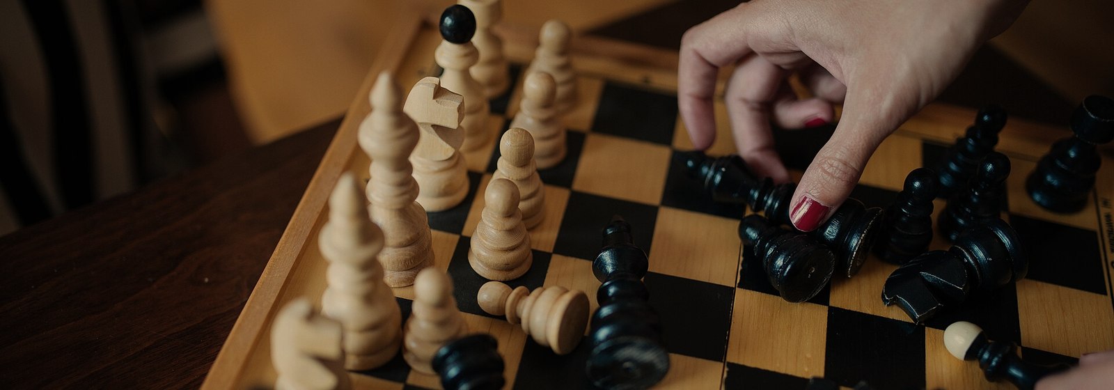 A hand moving a piece on a wooden chess board
