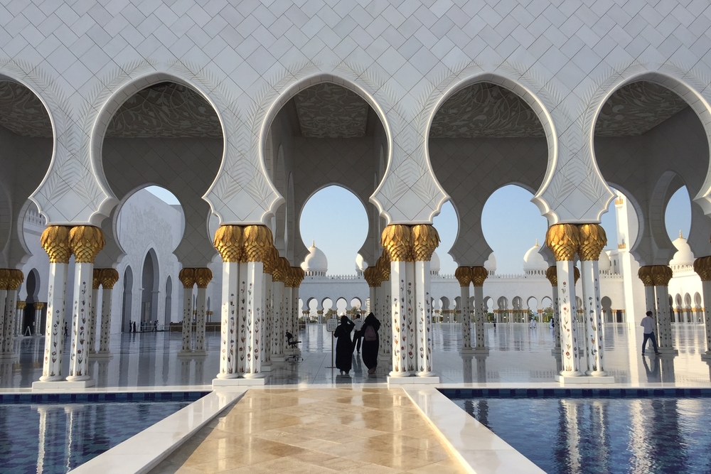 The arcade of the Sheikh Zayed Grand Mosque in Abu Dhabi, gold-capped columns reflected in the pool, photographed by Michael Olaiya