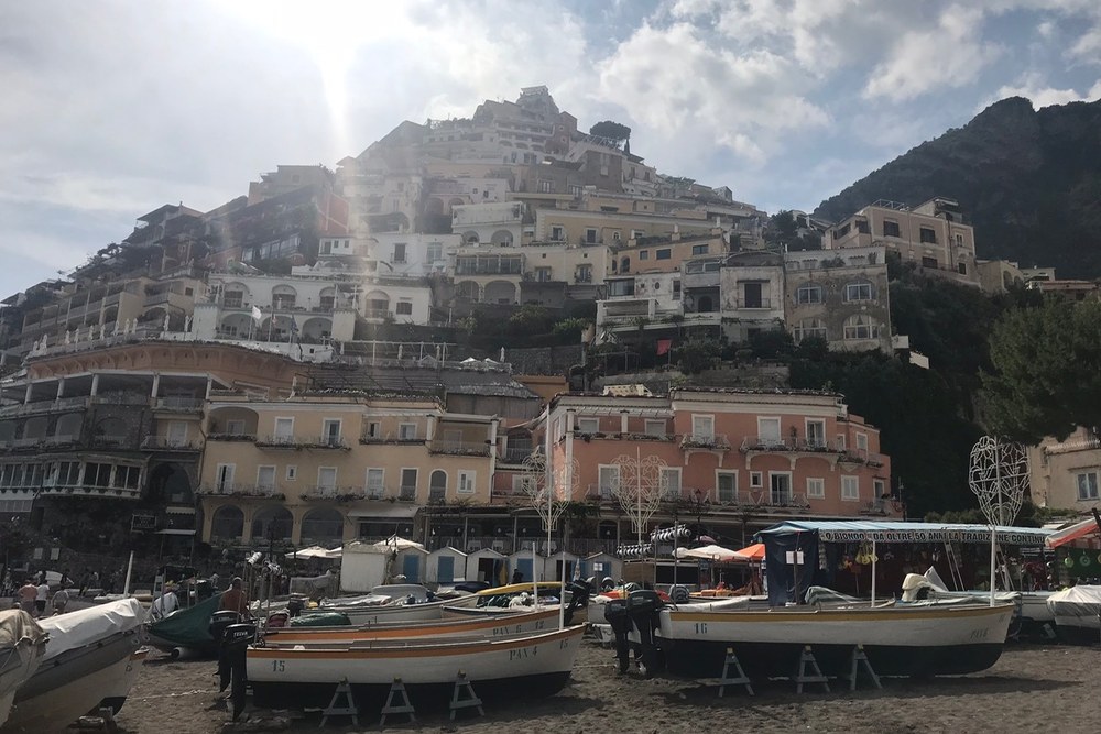 Fishing boats on the beach at Positano with the town stacked up the hillside behind, photographed by Michael Olaiya