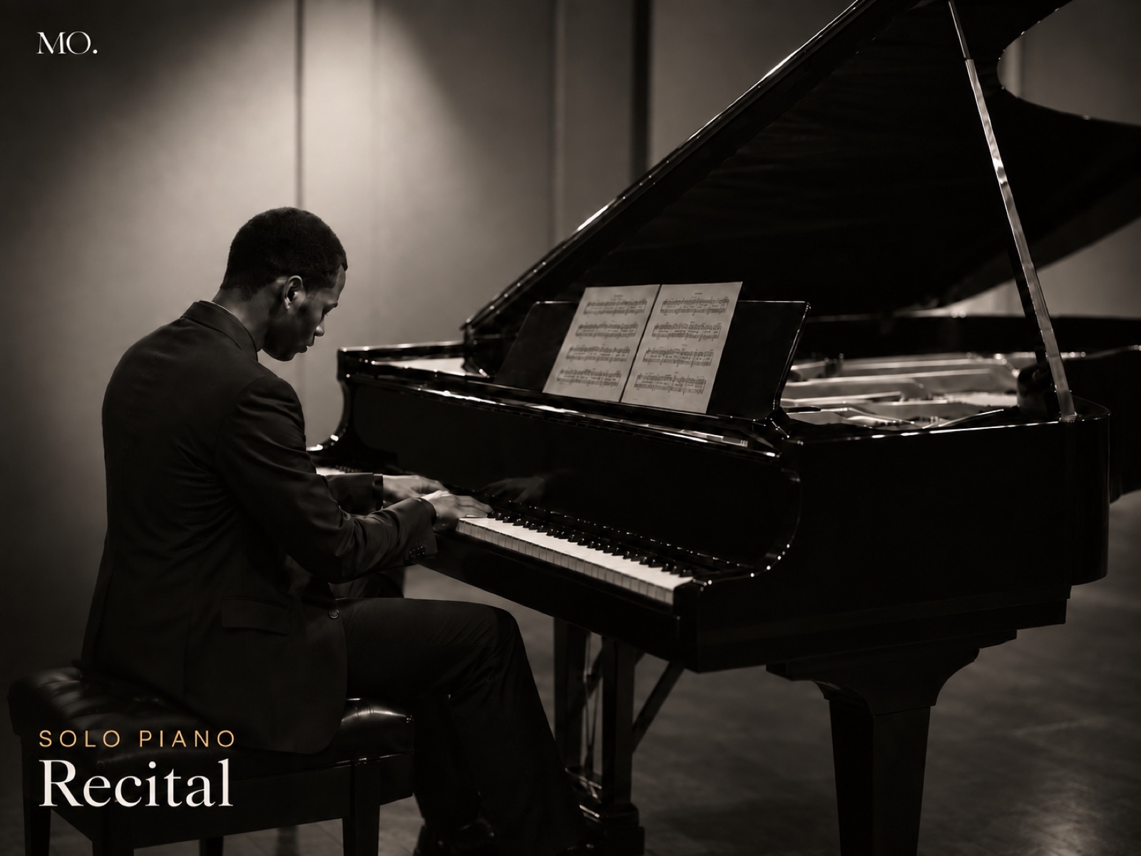 Michael Olaiya seated at a grand piano in a recital hall, in profile, playing from sheet music